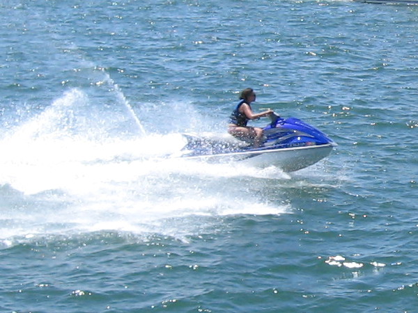 Someone zooms by riding a bucking water scooter over the sparkling blue water.