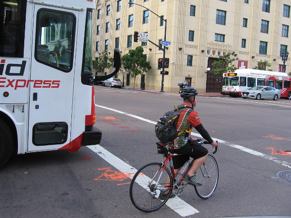 Morning commuter on a bicycle waits alongside a bus for a traffic light on Broadway.