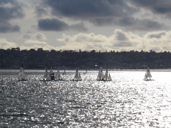 Small sailboats float on a sheet of silver, beneath dramatic clouds.