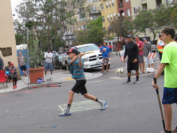 Young player on the Sidewalk Slammers team takes a swing during the early innings of a fungo-style stickball game.