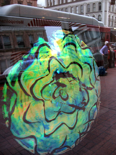 Unique holographic artwork painted on glass as seen through a Gaslamp window. Reflections of life on the street are also visible.