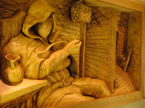 Amazing wood art. A hooded figure takes a break at an inn. Just Off The Road, Basswood, Randy Stoner.