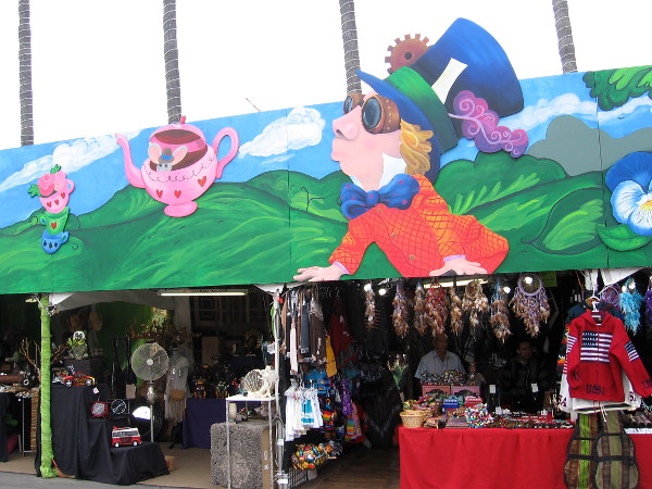 A long colorful mural above some fair vendors depicts beloved characters created by Lewis Carroll. Their appearance has evolved due to popular culture and now incorporate steampunk elements like goggles.