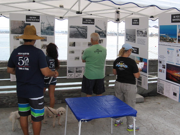 Visitors to the Ocean Beach Pier during its 50th anniversary celebration look at posters with information that concern the amazing concrete pier's construction and history.