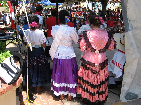 Beauty queens and dancers in colorful dresses watch the House of Peru lawn program in Balboa Park.