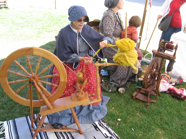 A lady in a bonnet at a spinning wheel was making wool yarn.