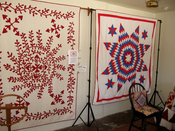 Two quilts on one wall greet visitors as they enter Threads of the Past. On the left is a modern version of the 1850s Juana Machado Quilt.