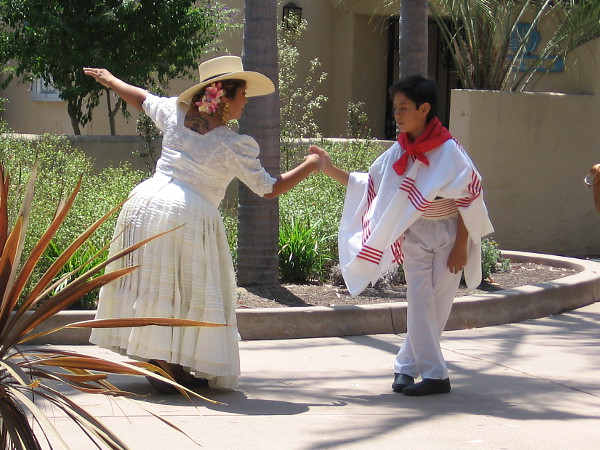 Costumed dancers, young and old, practice off-stage during the festive House of Peru lawn program in Balboa Park.