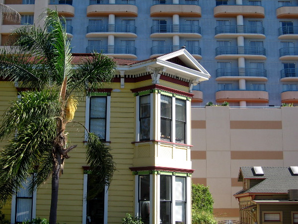 Morning sunlight slants in to touch the side of a newly painted Victorian house near a modern hotel.