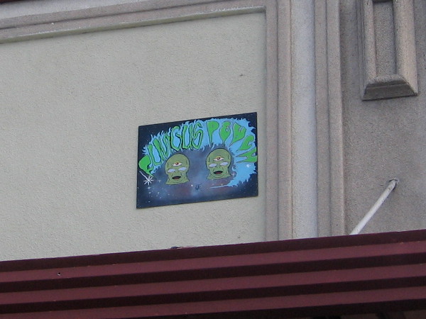 Unusual artwork near a building's rooftop features alien-like creatures with three eyes.