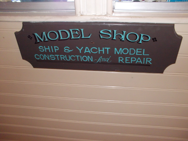 Ship and yacht model construction and repair. Sign beneath a window where museum visitors can watch craftsmen building small works of maritime art.