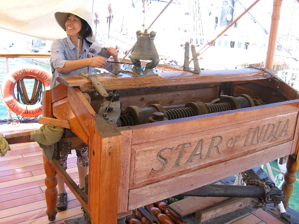 Visitor standing on the newly rebuilt poop deck of the Star of India rings the historic ship's bell. The wheel has been removed for refurbishment. The nearby binnacle and wooden benches will also be made like new!