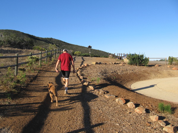 Early morning walker with dog on the Miner's Ridge Loop Trail, across a parking lot from the Trail For All People.
