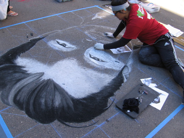 Another chalk artist at work creating a bold face in the middle of the street.