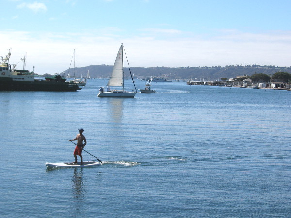 Sailboats, paddleboards and boats of every type out on blue San Diego Bay. The Pacific Ocean lies just beyond the peninsula of Point Loma, in the distance.