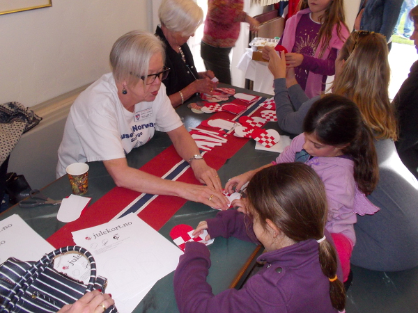 Inside the House of Norway, children make tiny paper Christmas baskets to hang on a tree among ornaments.