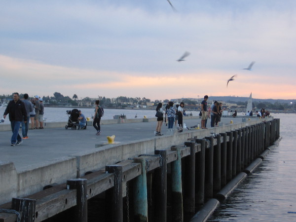 People stroll out on the pier near Seaport Village while gulls circle overhead and the sky changes color.