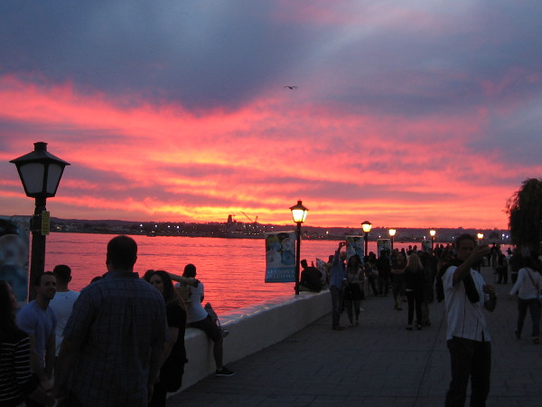 A glorious, glowing sunset turns the clouds orange and red. Visitors linger near the water at Seaport Village in San Diego.