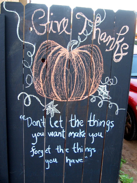 Chalk art wisdom on a city fence. Give Thanks. Don't let the things you want make you forget the things you have.