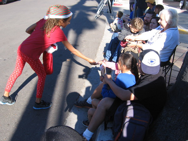 A young elf hands out Christmas candies to people watching La Jolla's joyful holiday parade.