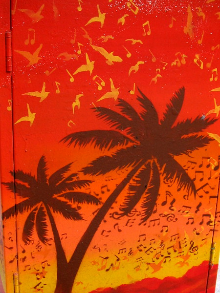Musical notes and birds fly among tropical palm trees. An image on a utility box warms the city as winter nears.