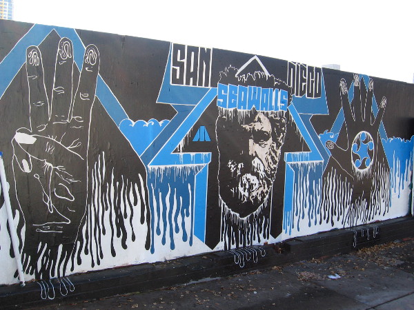 A San Diego Sea Walls mural on the same wall features a bearded face and two hands. Not sure about the symbolism.