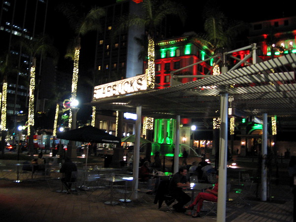 People sit at tables near the outdoor Starbucks at Horton Plaza Park one early mid-December evening.