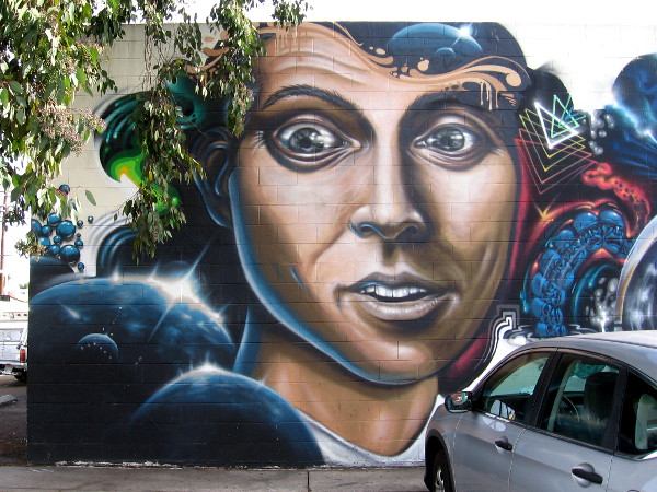 A wide-eyed human face on a wall in North Park, surrounded by cosmic imagery.