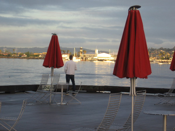 Someone gazes from the Broadway Pier across the water toward Coast Guard Air Station San Diego, whose buildings shine, reflecting the early morning sun.