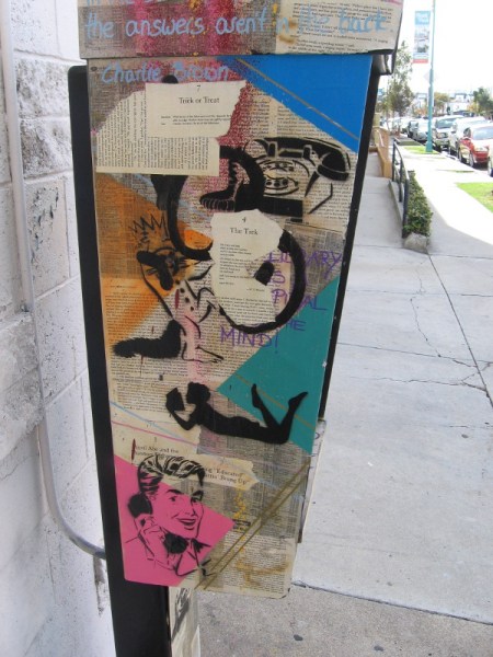 Artistic collage on a public telephone includes the printed word, and various stencil faces and figures.