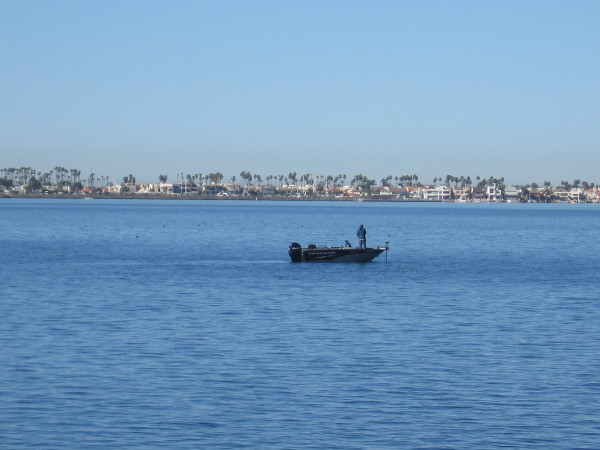 A fisherman out on San Diego Bay. The Coronado Cays are visible across the calm blue water.