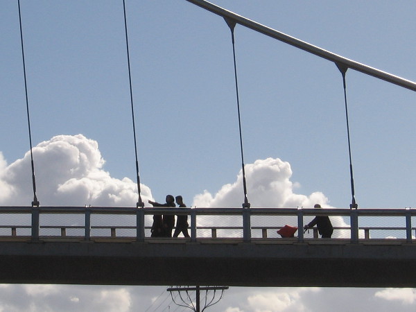 People crossing the Harbor Drive pedestrian bridge seem to walk in the clouds