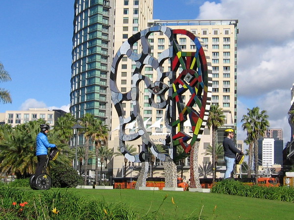 Tourists on Segways pass the Coming Together sculpture by artist Niki de Saint Phalle.
