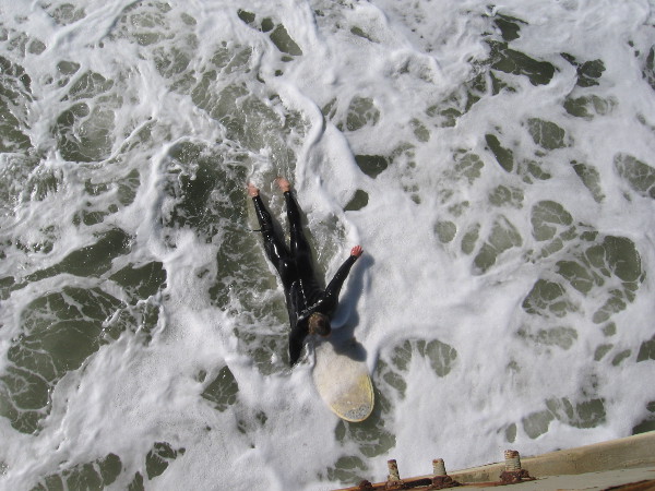 Surfer in a wetsuit about to paddle under the pier.