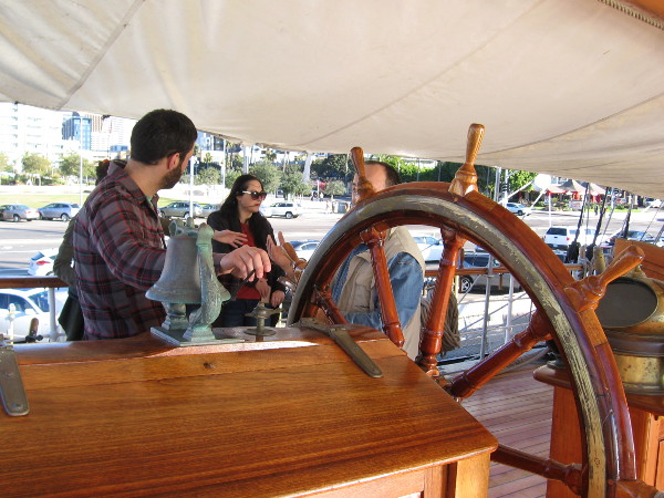 A visitor rang the ship's cheerful bell while his friends talked near the binnacle and helm.