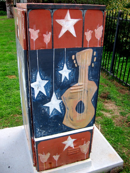 A guitar and stars decorate a utility box.