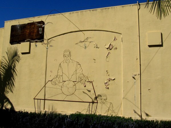 I spotted this cool metal wire sculpture of a man dining on the planet Earth near an old, peeling Naval Training Center wall. The art includes a dangling mobile and casts a thin, weird shadow.