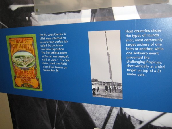 Early year displays include a 1904 program for the Louisiana Purchase Exposition and an early version of archery competition where the bird target sat atop a 31 meter pole.
