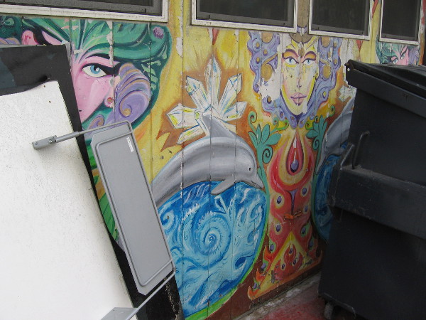 Cool street art faces in a Mission Beach alley peer from behind trash bins.
