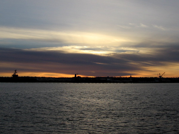 The sun is setting across San Diego Bay above Navy ships docked at North Island.