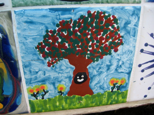 Colorful tiles painted by many creative hands form a mosaic on the Envirocan's other three sides. Here's the face of a happy critter in a tree, and some flowers.