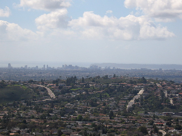 A zoomed photo. Downtown skyscrapers rise beside San Diego Bay. The Point Loma peninsula can be seen, as well.