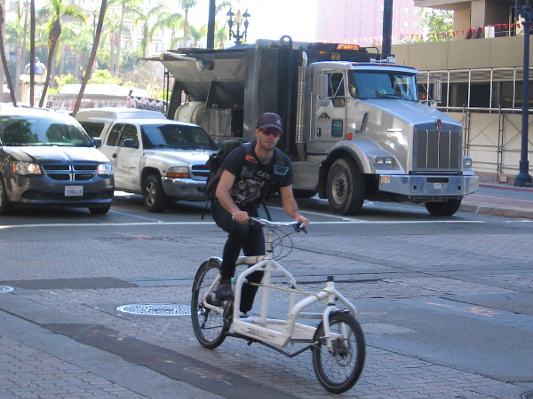 Here comes a guy riding a cool bicycle that appears to be designed for deliveries.