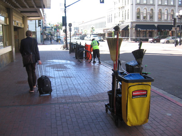A worker with Clean and Safe's downtown program mops the sidewalk while a businessman walks by.
