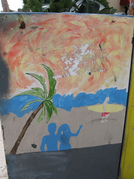 A typical beach scene with sand, palm tree and surfer.