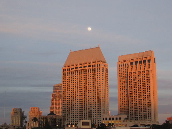 The Manchester Grand Hyatt towers turn golden in the last rays of the sun. A nearly full moon rises above them.