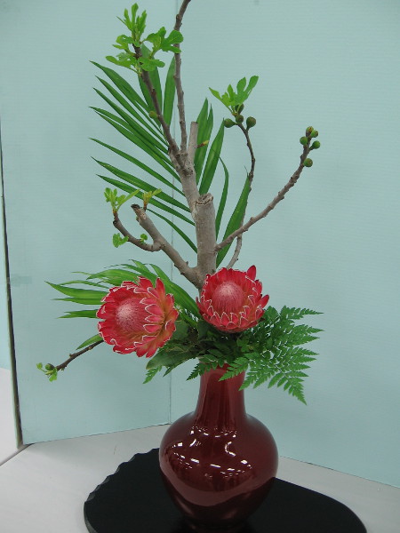 Freestyle arrangement by Mitsuko Takeya. Materials include fig branch, protea, palm leaves and leather fern.