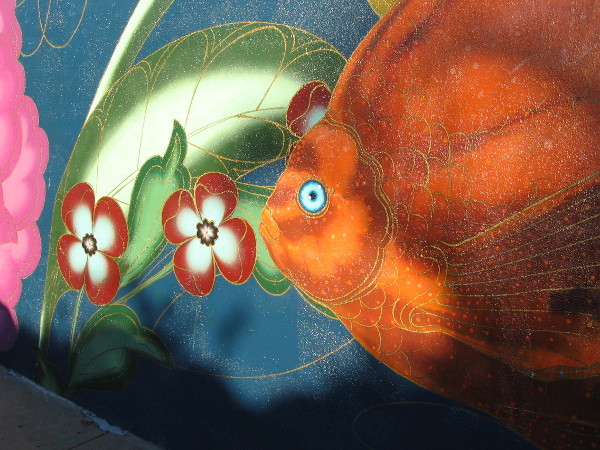 A bright orange fish swims past jewel-like flowers.