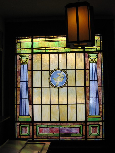 Stained glass shows classical columns and a cross in a crown.