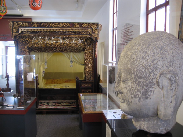 Looking past the Buddha head at a fantastic, ornate alcove bed.